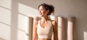 A smiling woman with curly hair in athletic wear, lit by soft natural light, representing the energy and vitality women pursue through bioidentical HRT.